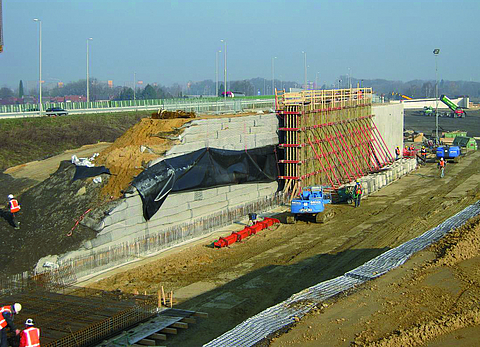 A construction site with several workers and various machines carrying out earth pressure relief and bridge abutment work.