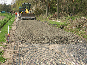 Gravel is spread on the Basetrac Grid by workers and construction machinery