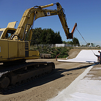 Excavator uses a laying traverse to roll out Tektoseal® Clay bentonite mats