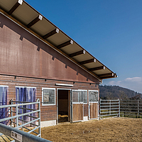 Stable building with Lubratec brown windbreak net for improved stable climate