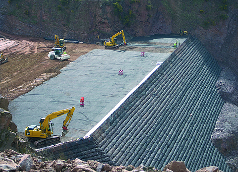 The slope is being excavated layer by layer using an excavator