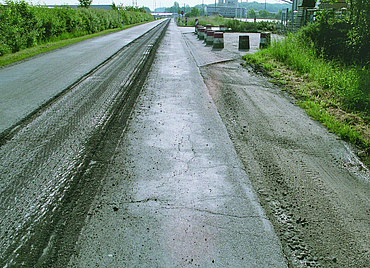 A road with milled-out sections and damage in an outdoor area