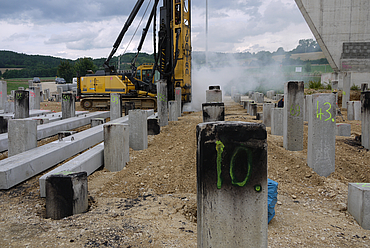 Precast concrete driven piles being worked on by an excavator