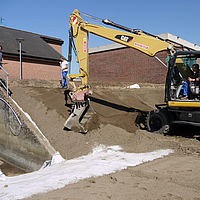 Excavator spreads soil over Tektoseal® Clay bentonite mats to stabilize a small slope