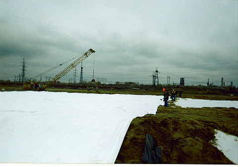 Construction site of a sewage sludge disposal basin, with an excavator and workers