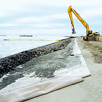 A dredger covers installed erosion control mats with the help of riprap revetment on the seashore